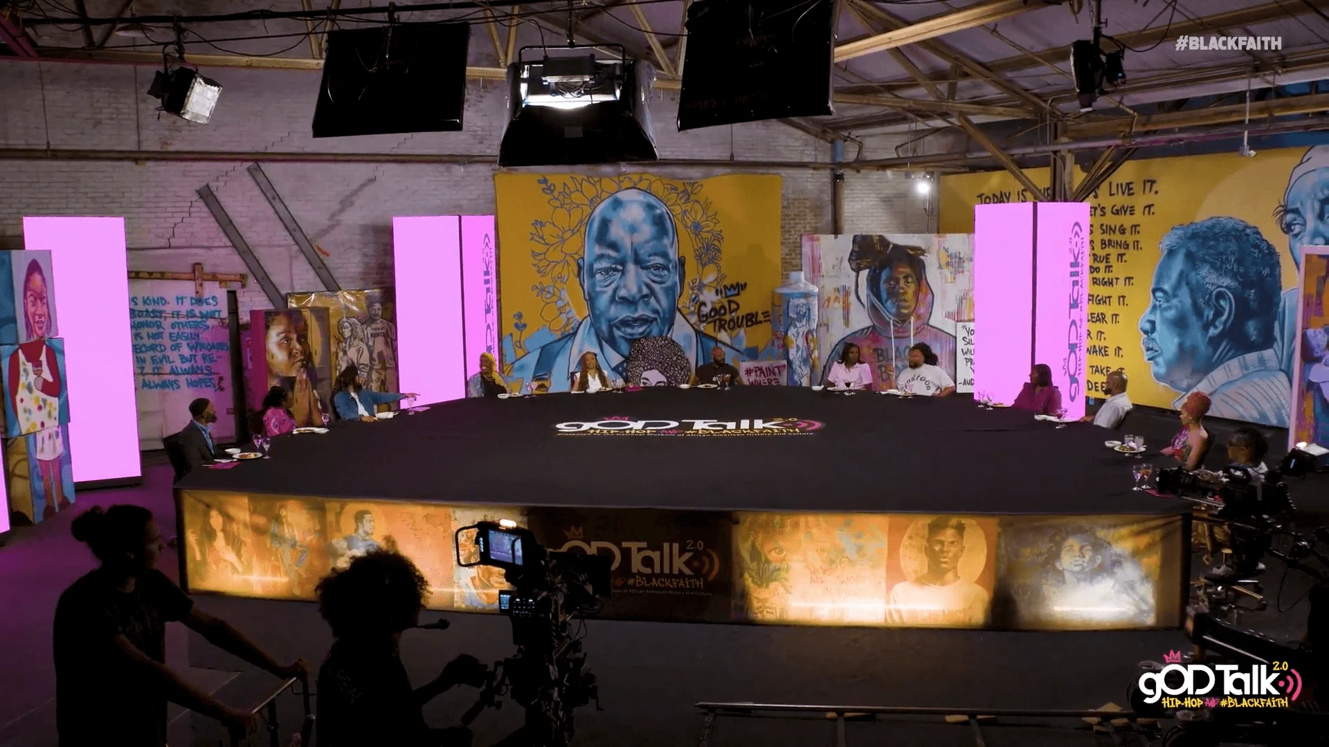 The gODTalk 2.0 set, a round table under studio lights surrounded by murals.