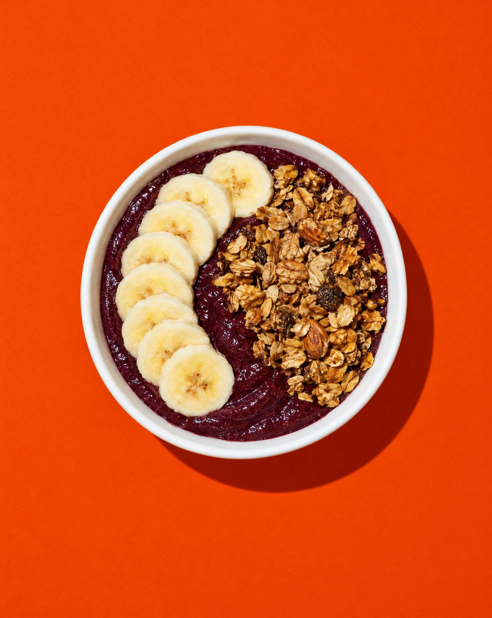 An açaí bowl with banana and granola on an orange backdrop.