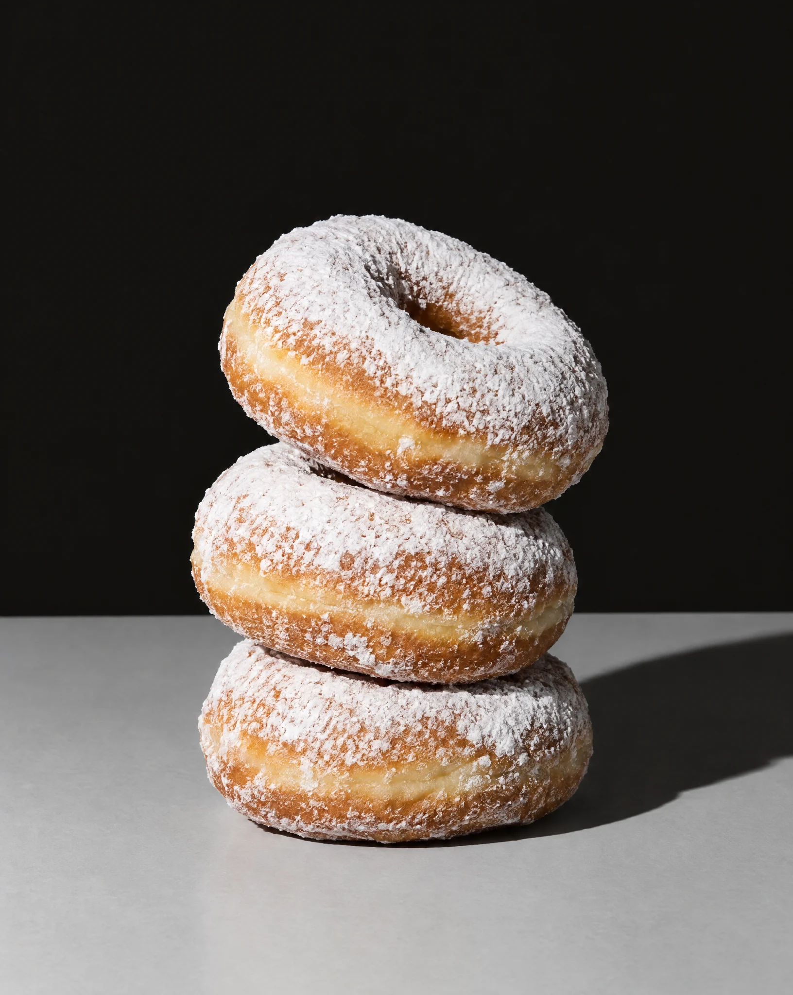 Three powdered donuts stacked against a black backdrop.
