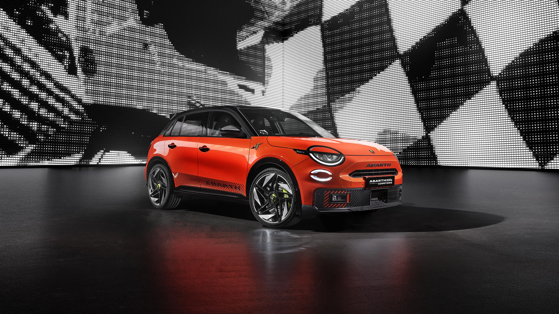 Orange-schwarzer Abarth 600e Competizione vor einer beleuchteten Wand