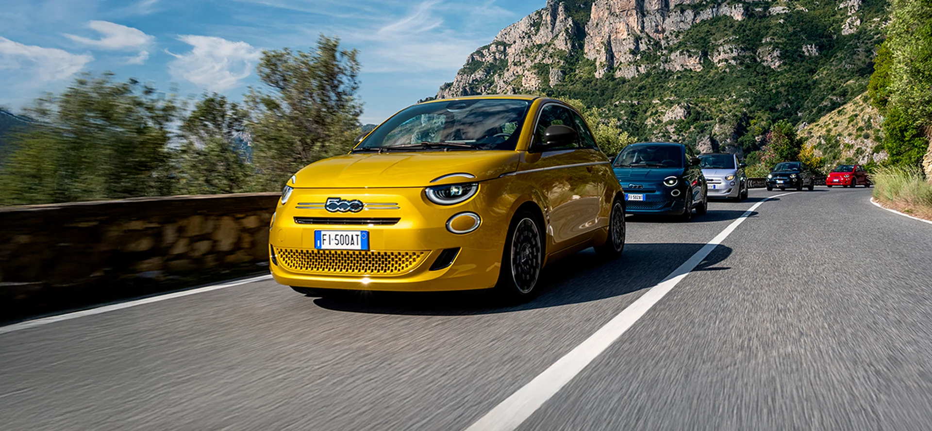 Gelber Fiat 500 Hybrid auf einer Bergstraße mit weiteren Fiat 500 im Hintergrund