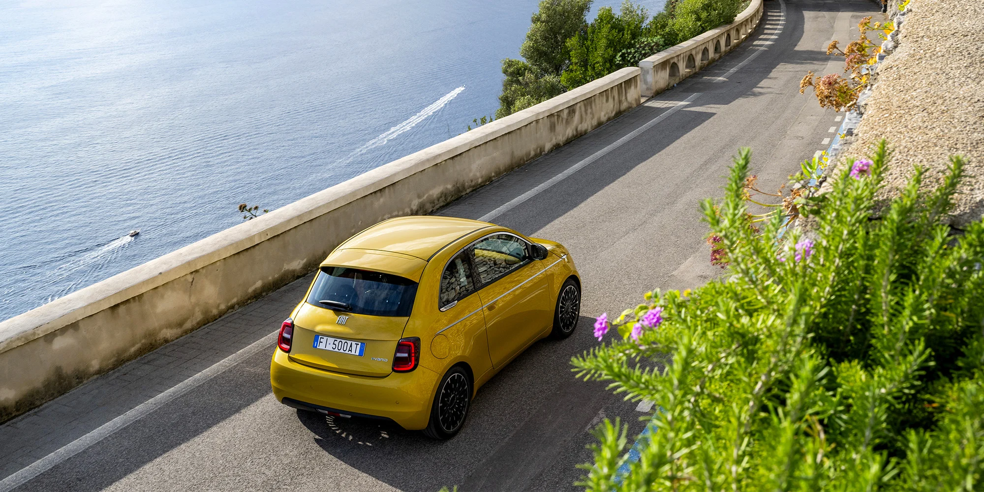 Gelber Fiat 500 Hybrid auf einer Küstenstraße, von hinten fotografiert