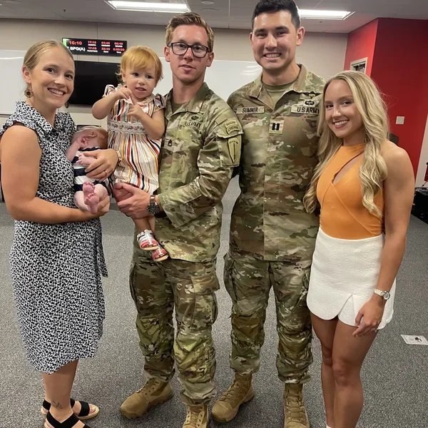 Derrick in Army uniform with Emily, a fellow soldier and his family at a unit event.