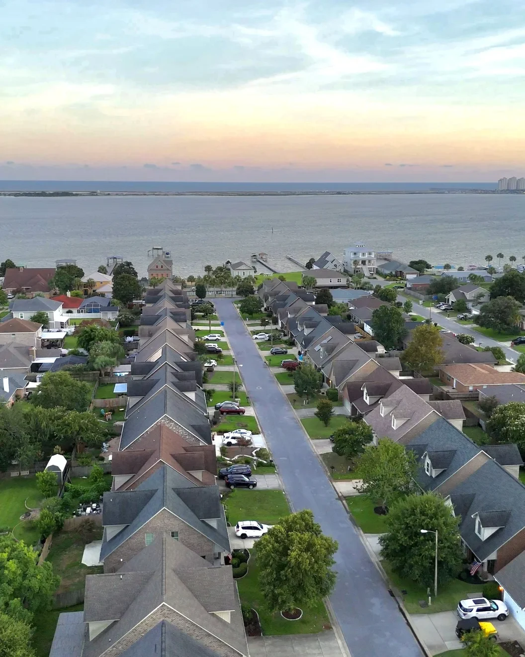 Aerial view of a tree-lined residential street leading to the Sound, with the Gulf and island condos on the horizon at sunset.