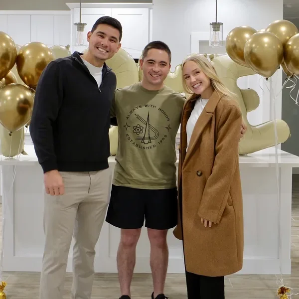 Derrick, Emily and a client in a kitchen decorated with gold balloons.