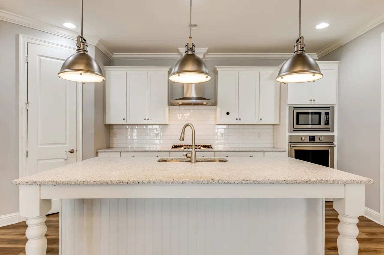Bright white kitchen with a large island, three pendant lights, subway tile backsplash, range, sink, and built-in appliances.