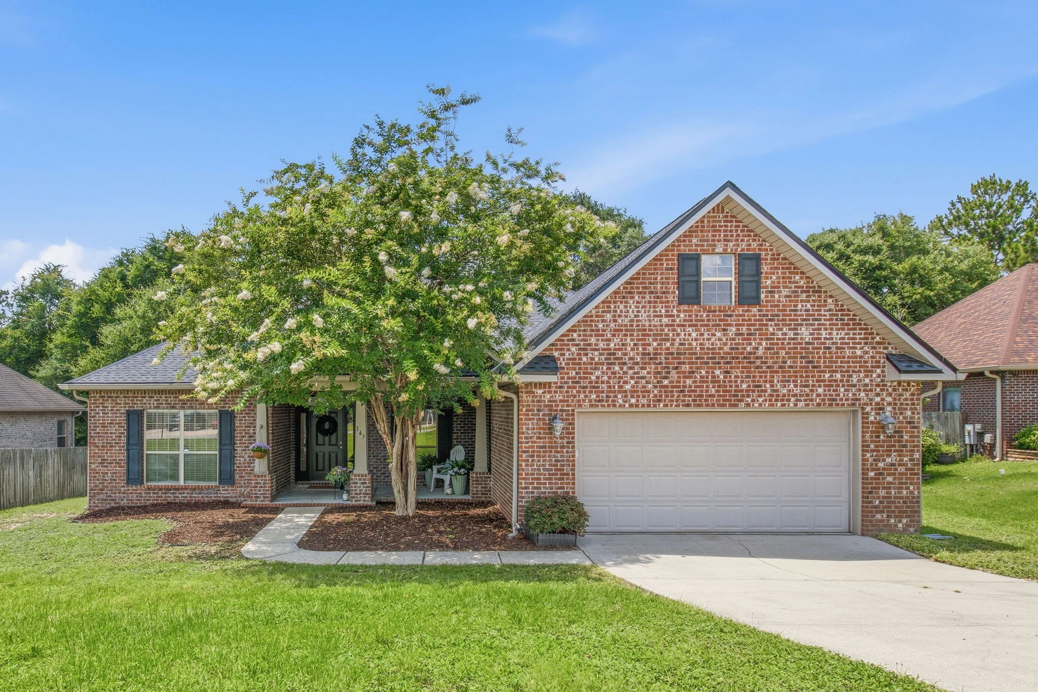 Red-brick suburban house with a flowering tree, garage, front porch, lawn, and concrete driveway.