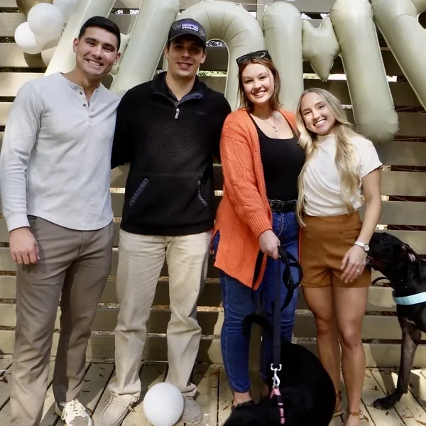 The Sumners celebrate with new homeowners and their dog on a deck with balloon letters.