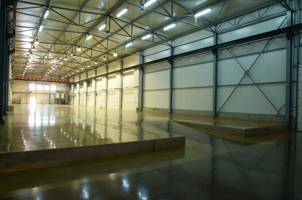 Reflective concrete floor beneath steel roof trusses in a large industrial interior