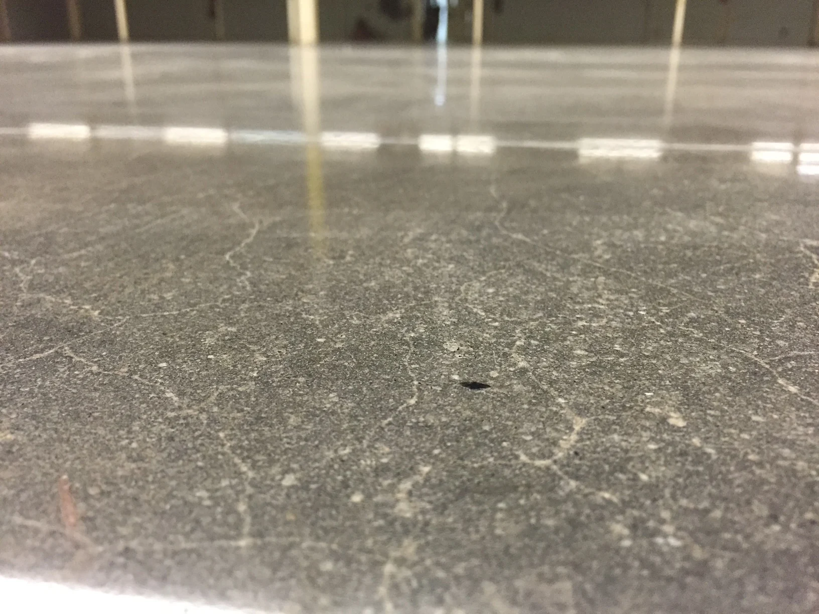 Close-up of a reflective concrete surface with visible aggregate, fine marks, and a small surface pit