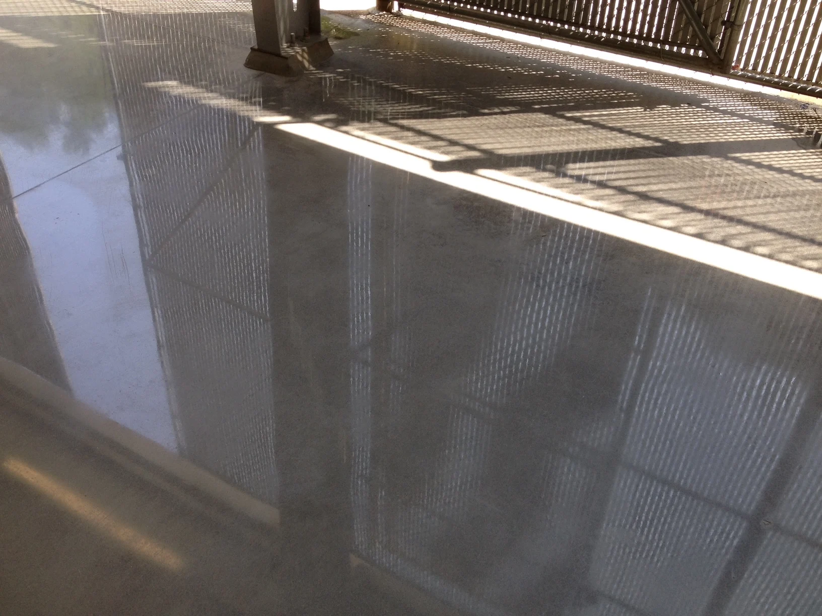 Reflective concrete floor beneath a covered structure beside a wooden fence