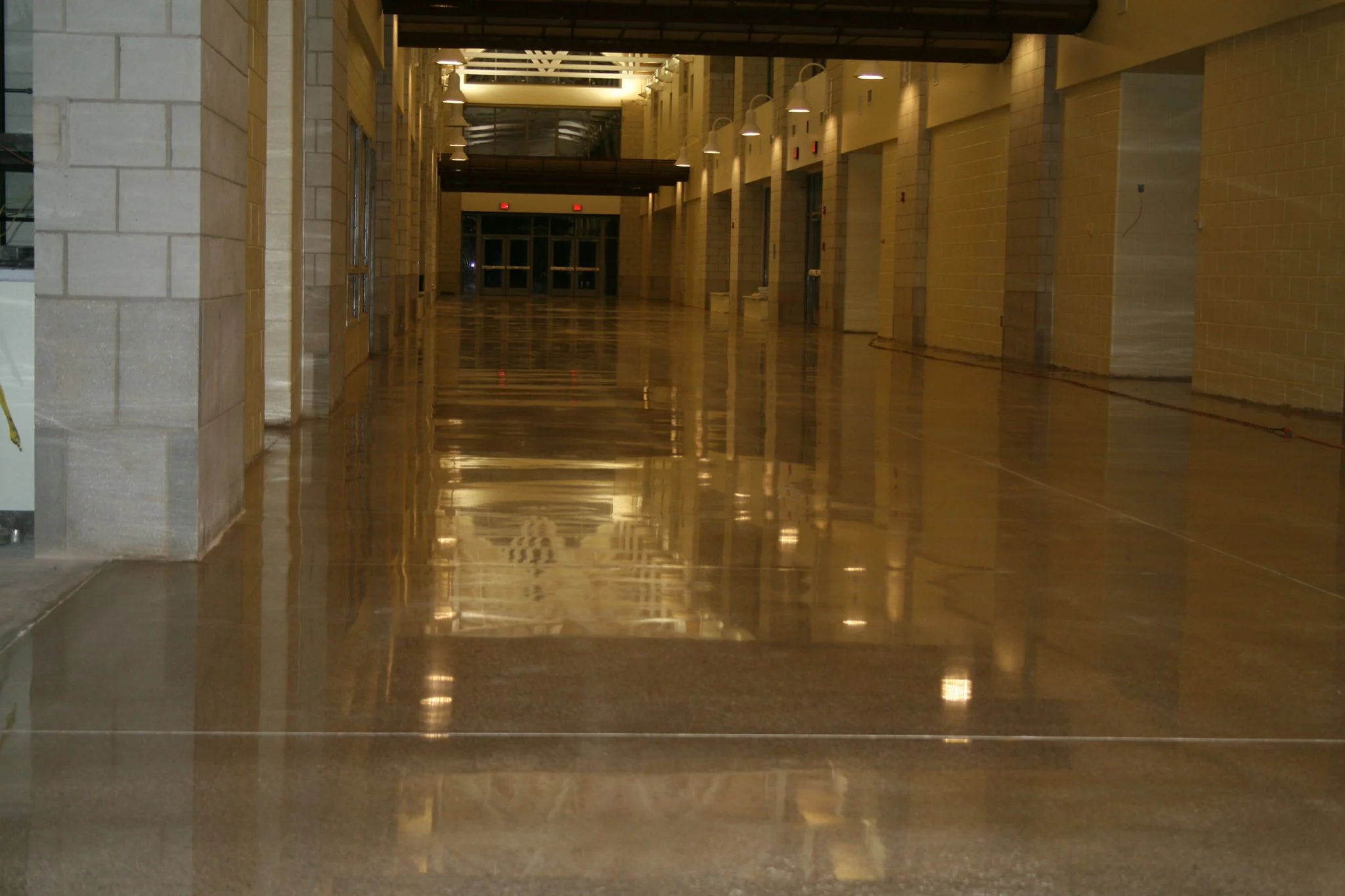 Reflective warm-brown concrete floor in a corridor with block walls and overhead lights