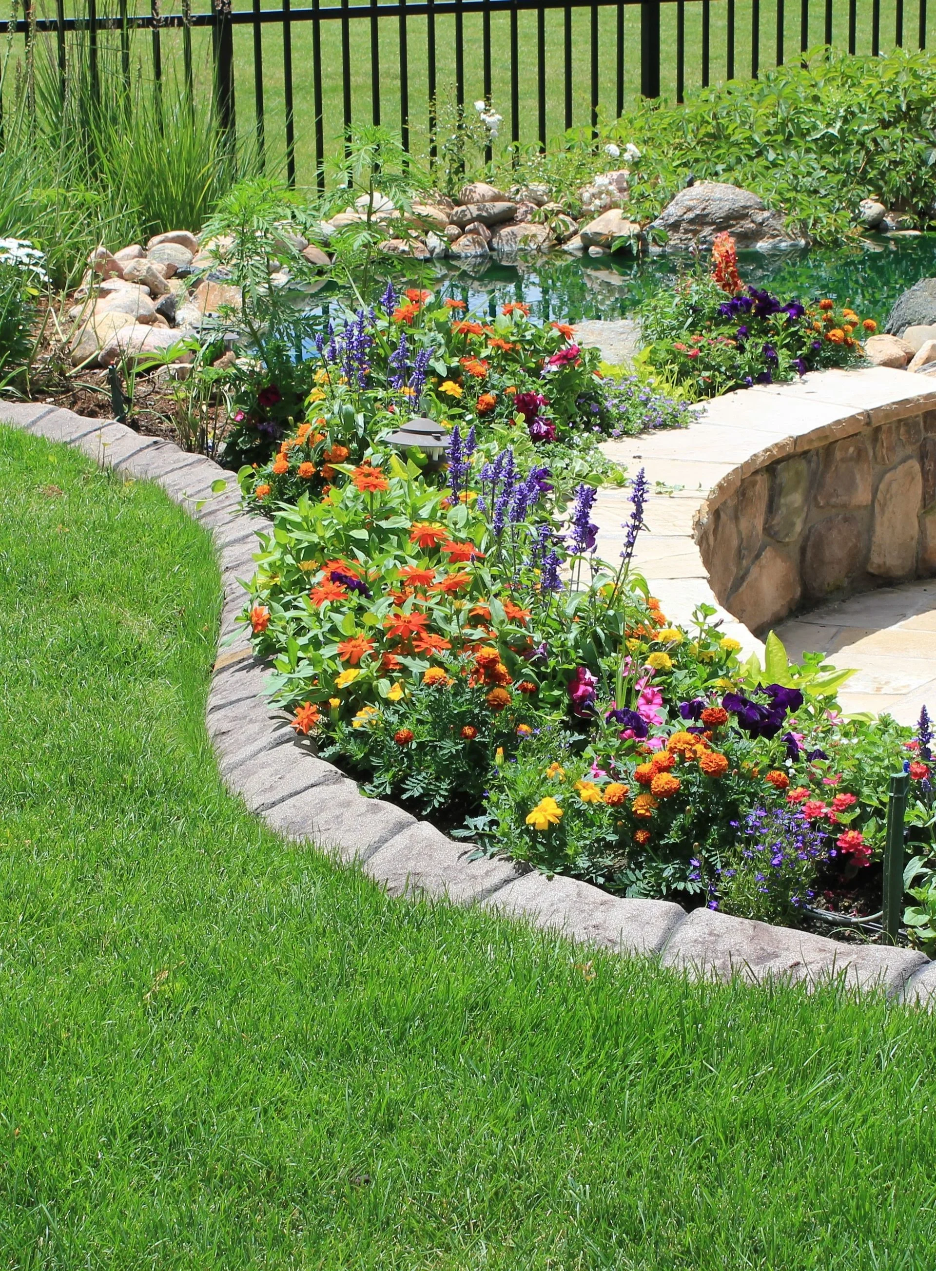 Concrete curbing around a colorful flower garden and pond