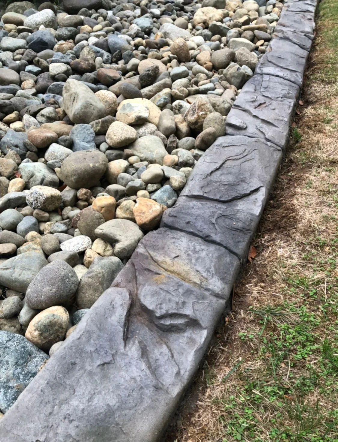 Textured concrete curbing containing a river rock landscape bed
