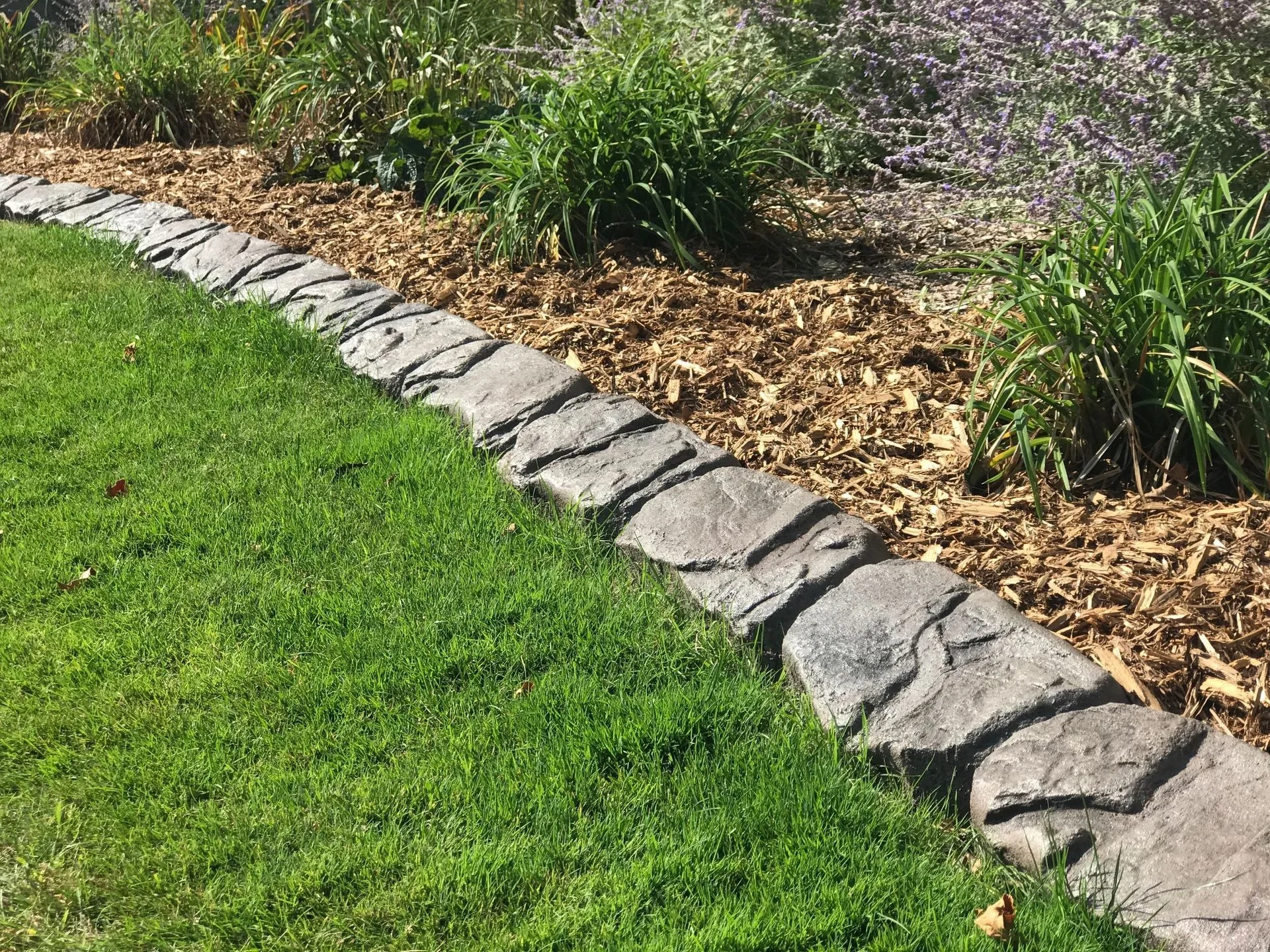 Decorative stone curbing between a lawn and mulched garden bed