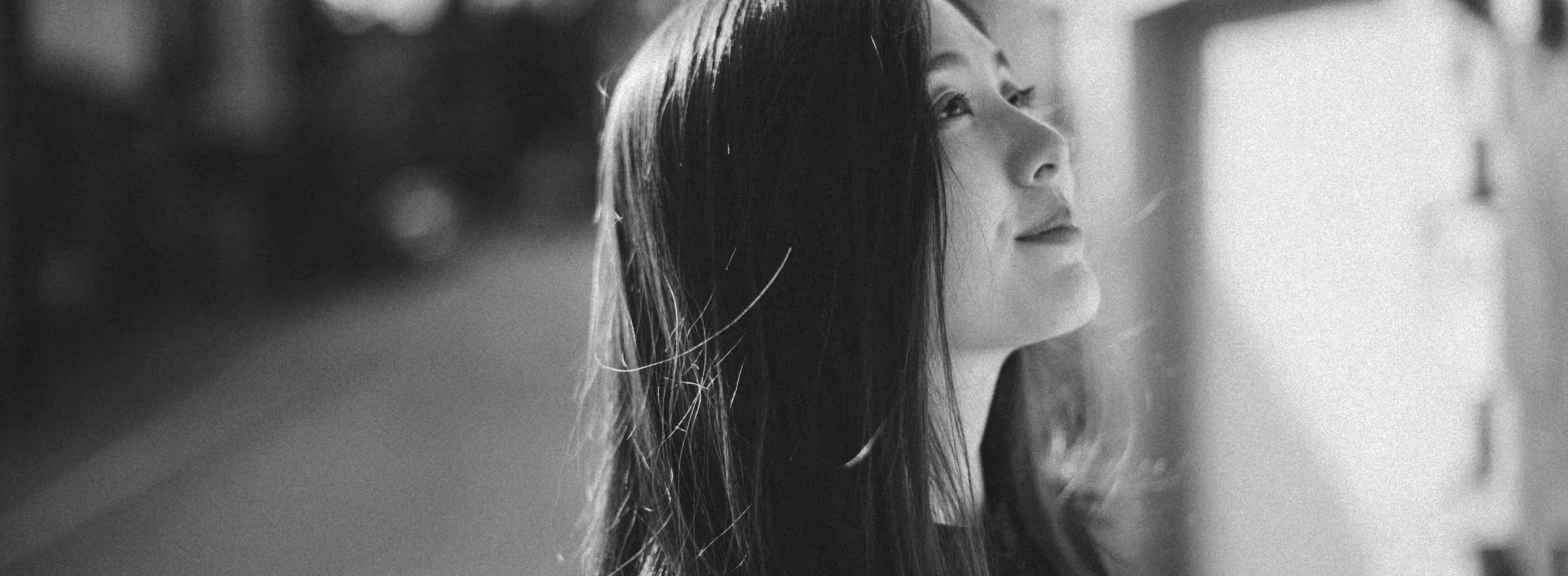 Black and white side profile of a woman with long hair looking upward, blurred background.