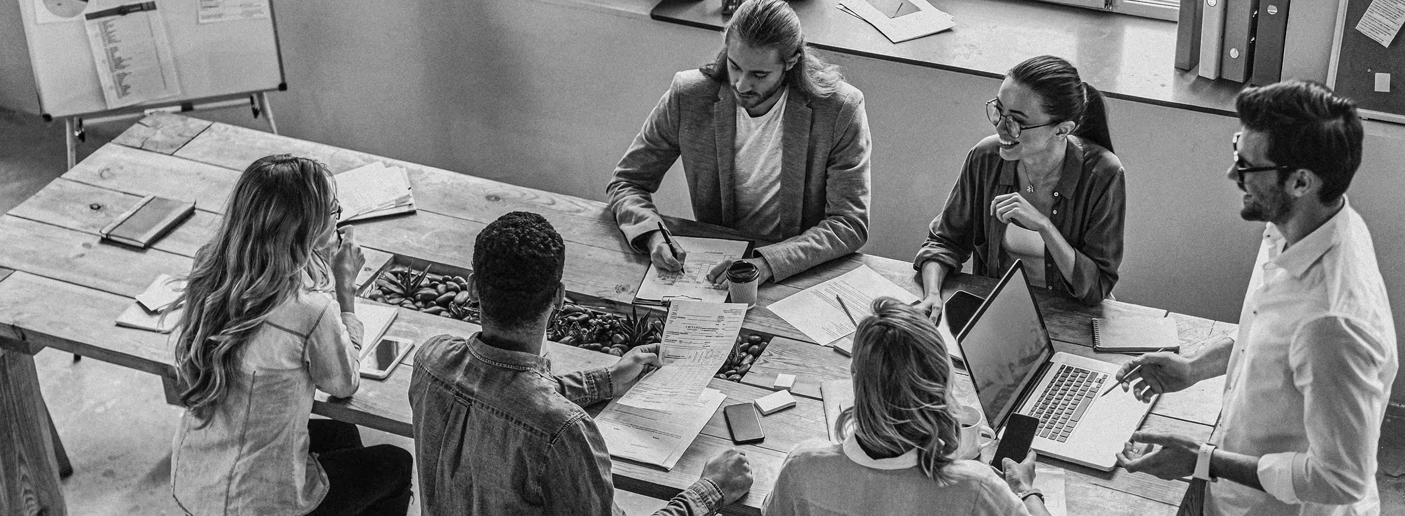 Five people sitting and standing around a table engaged in a collaborative office meeting.
