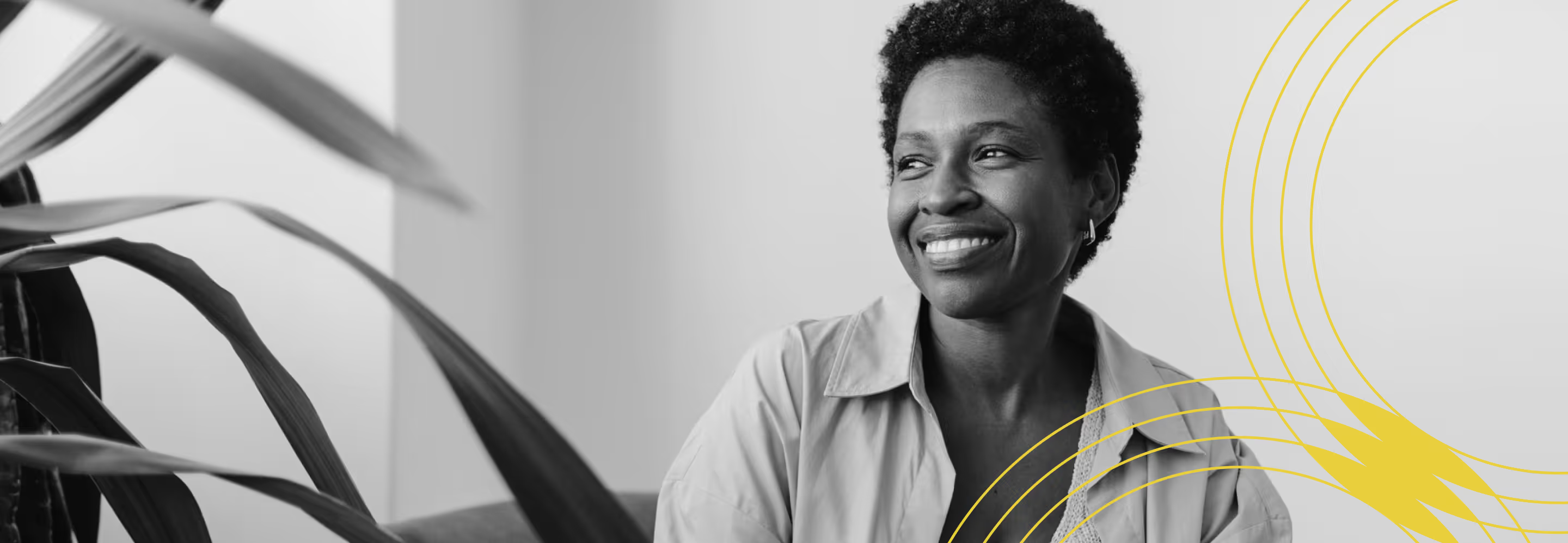 Smiling woman with short hair sitting indoors near a plant and yellow graphic lines on the right.
