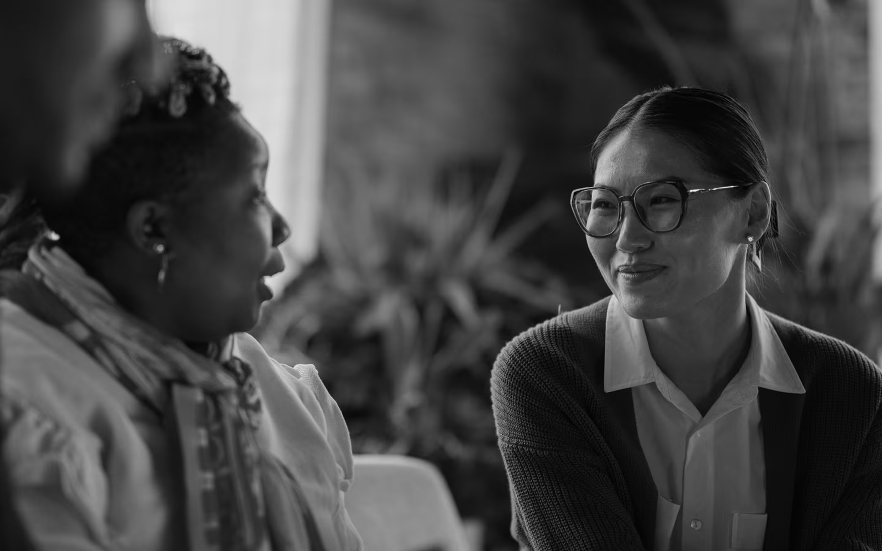 Two women engaged in conversation, one wearing glasses and smiling, the other speaking with expressive gesture.