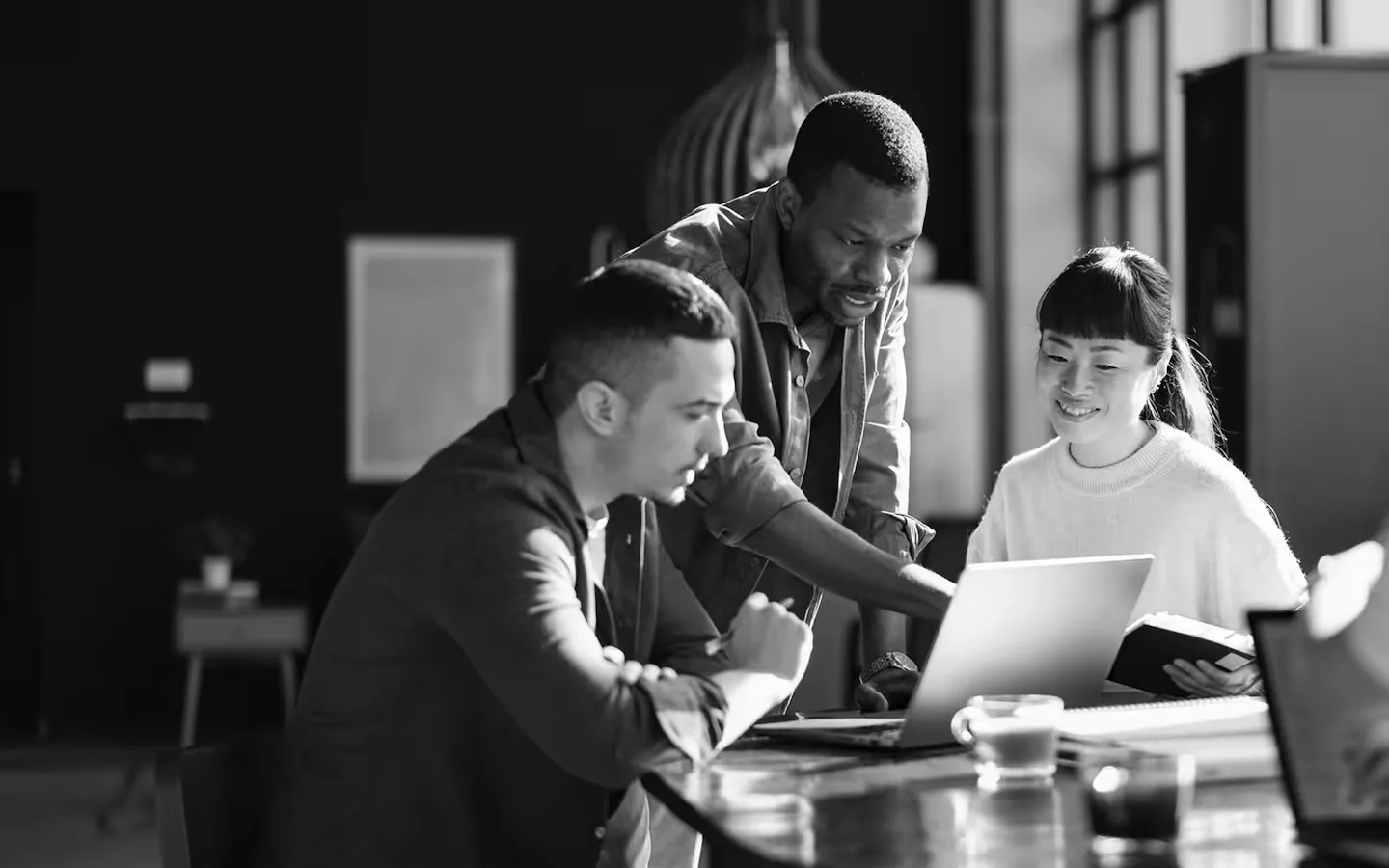 Three colleagues collaborating around a laptop at a table in a modern office.