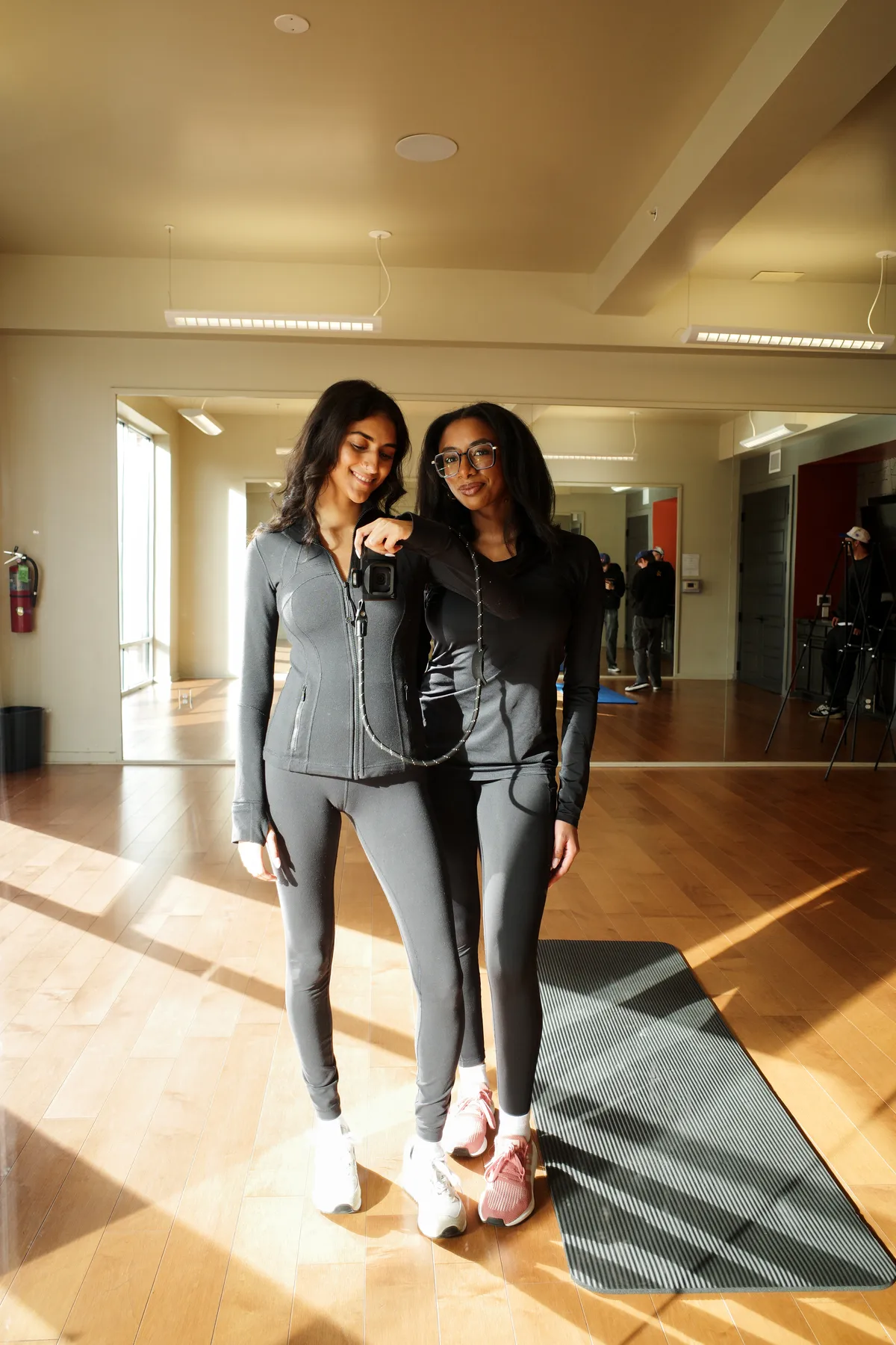 Two talent on a Studio + Commerce lifestyle shoot in a fitness studio, with crew and a tripod in the background