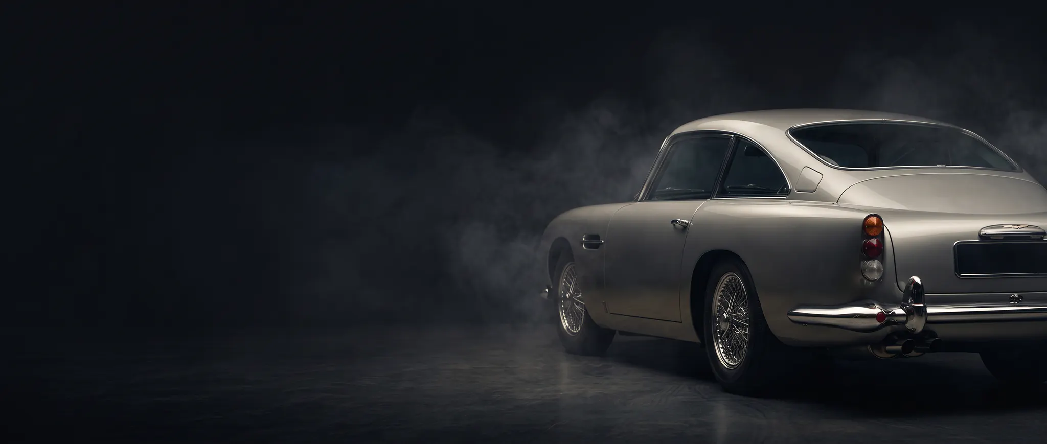 Rear view of a silver classic Aston Martin in a dark studio