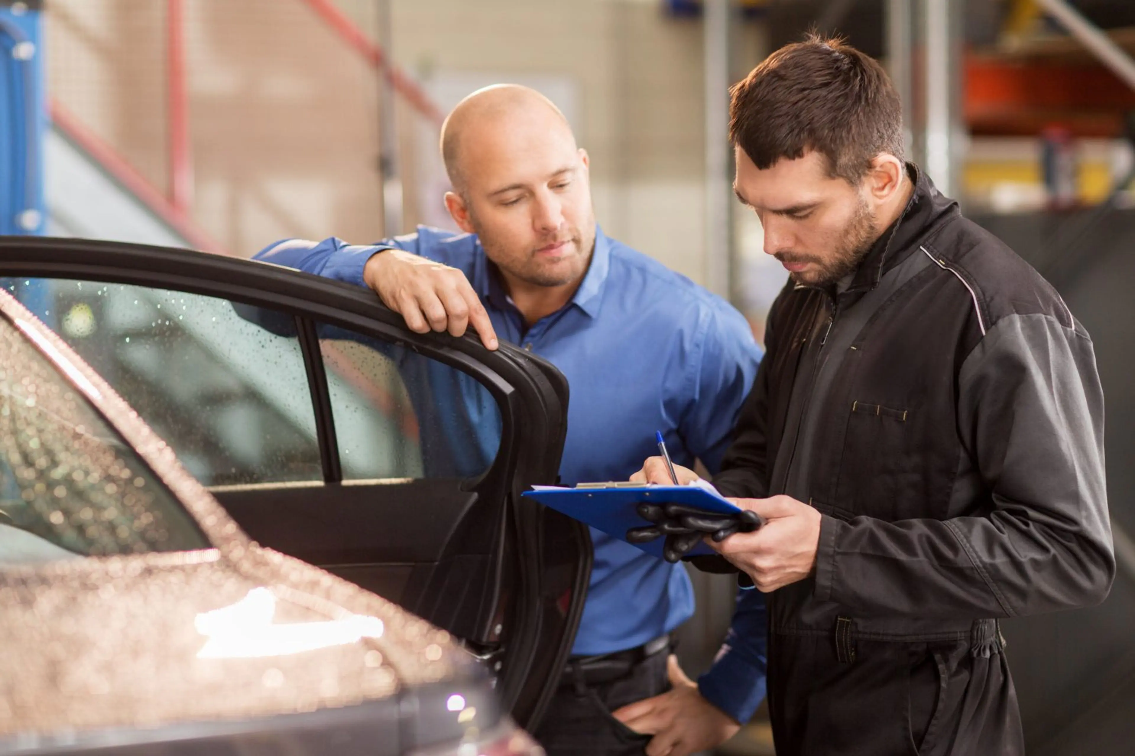 Auto service advisor and mechanic inspecting a car and filling out a work order in a repair shop