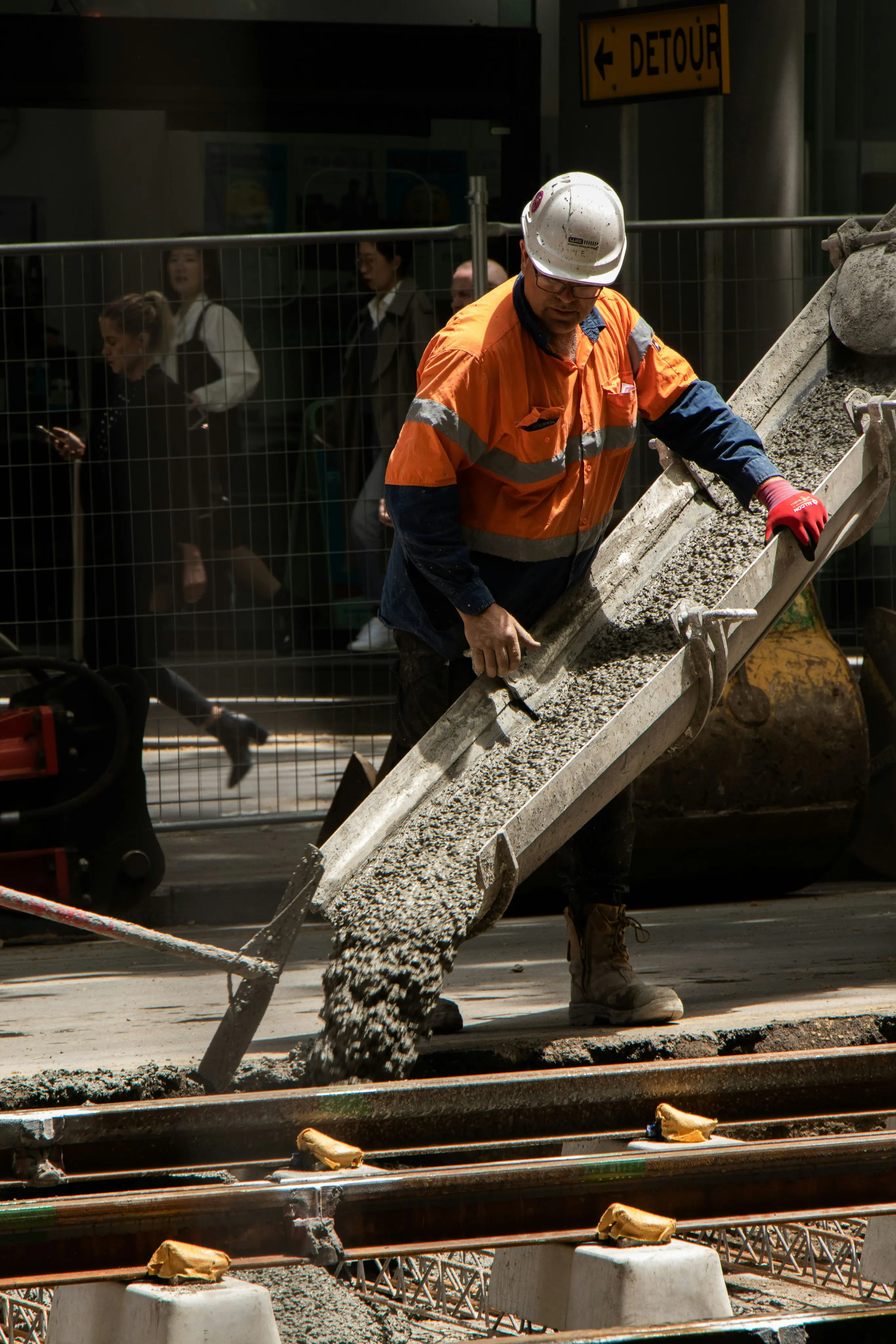 Construction worker in high-visibility gear pouring concrete at a street work site