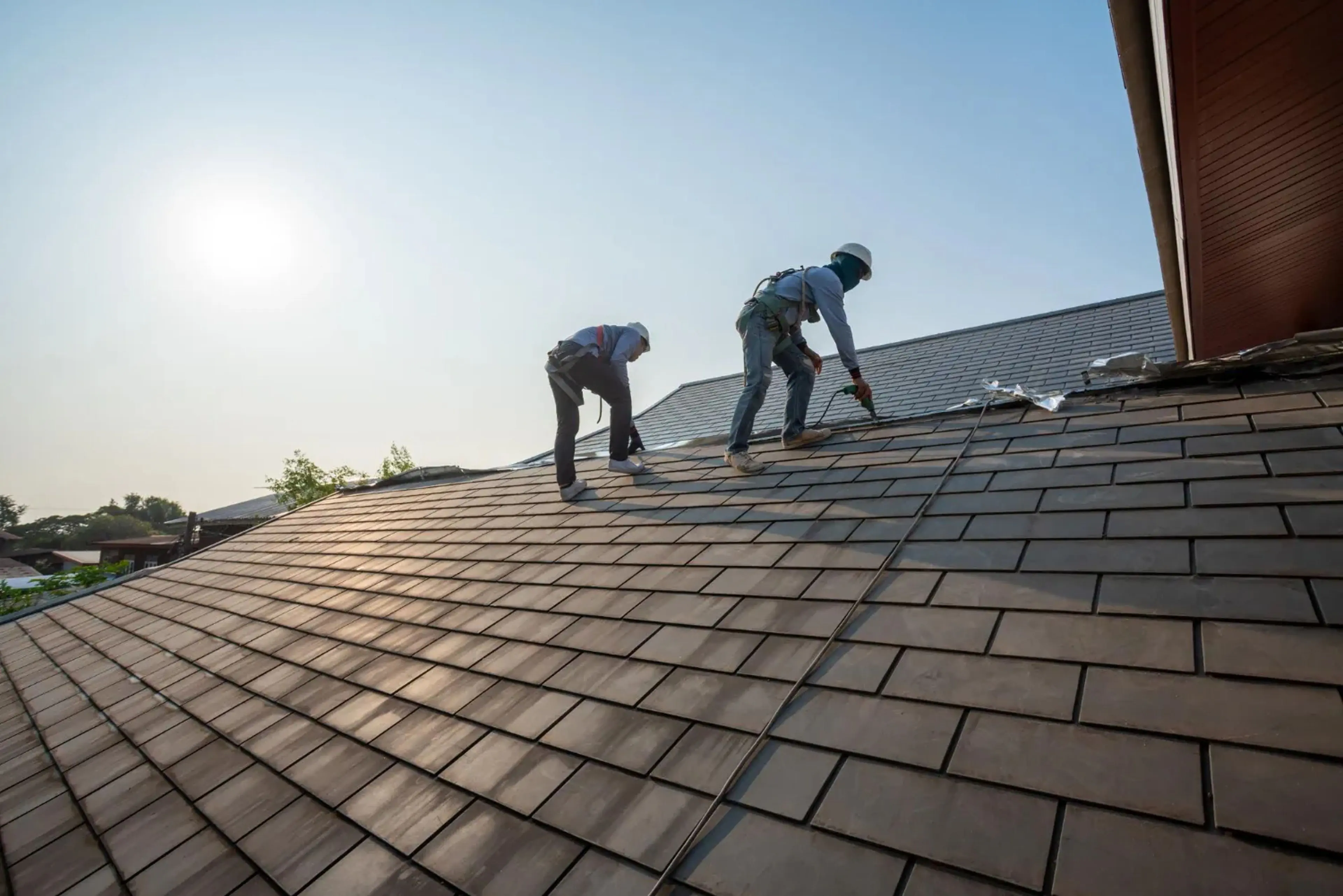 Two roofers installing tile shingles on a residential roof at sunset