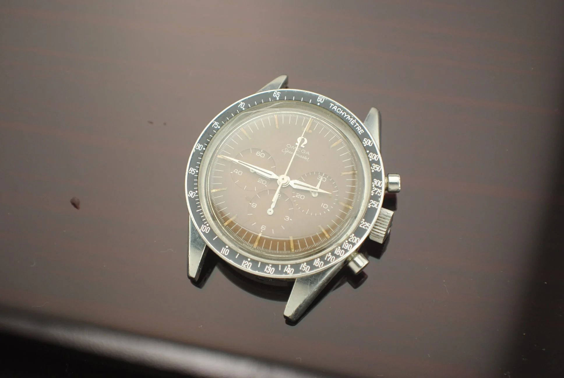 Crystal-on view of the sold Omega 2915 tropical-brown chronograph watch head resting on a dark surface