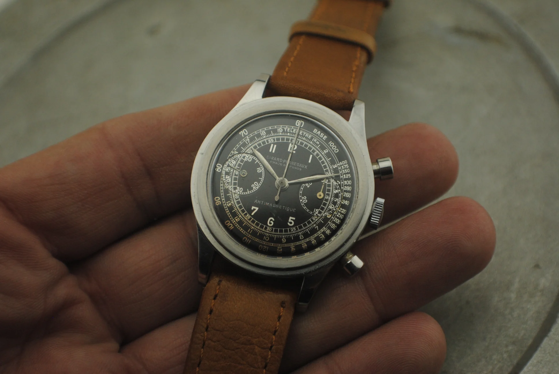 Crystal-on in-hand view of the Girard-Perregaux stainless-steel stepcase chronograph with silver galvanic multi-scale dial and brown leather strap