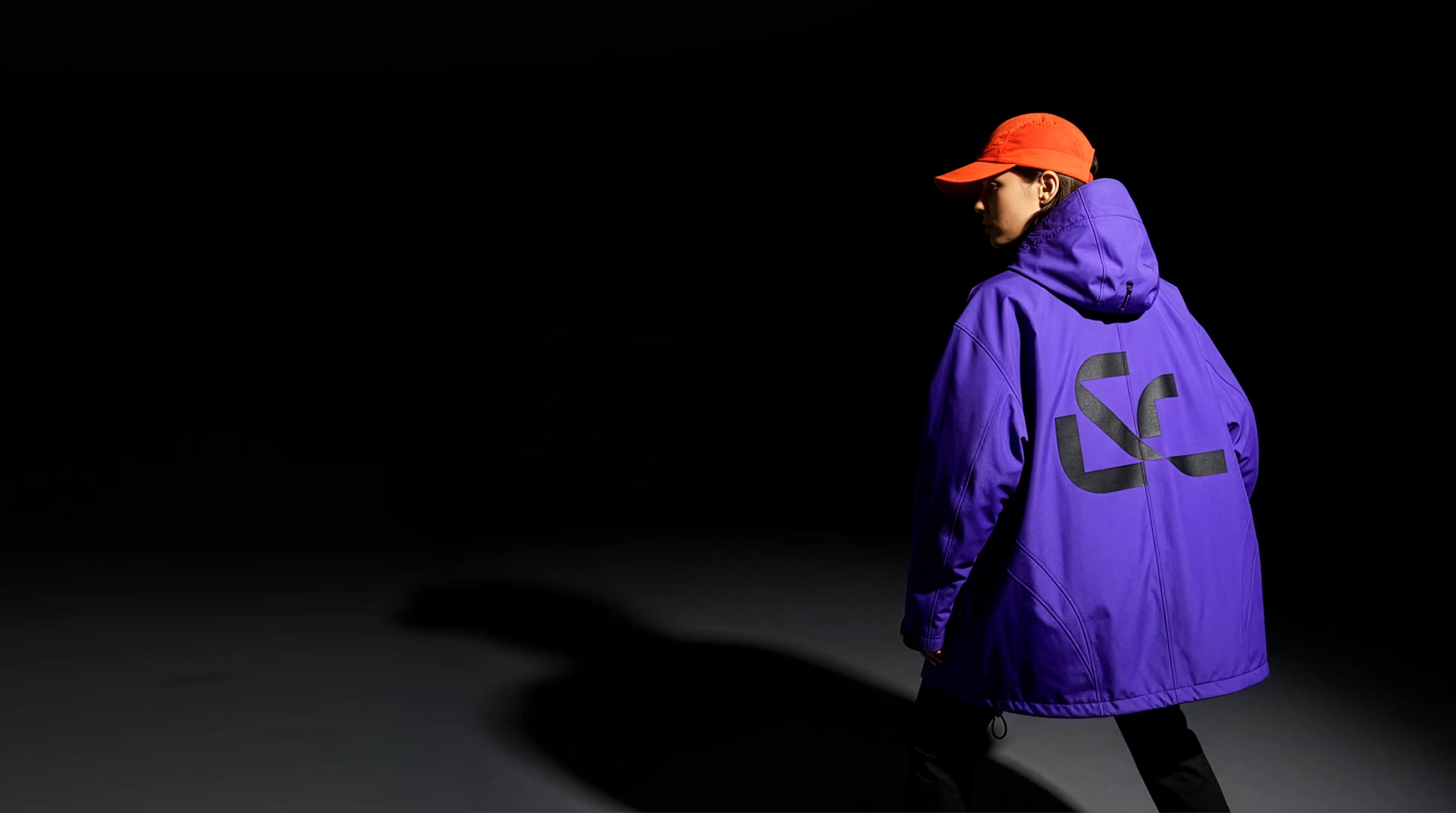Person wearing a violet Stitch jacket and an orange cap against a dark background