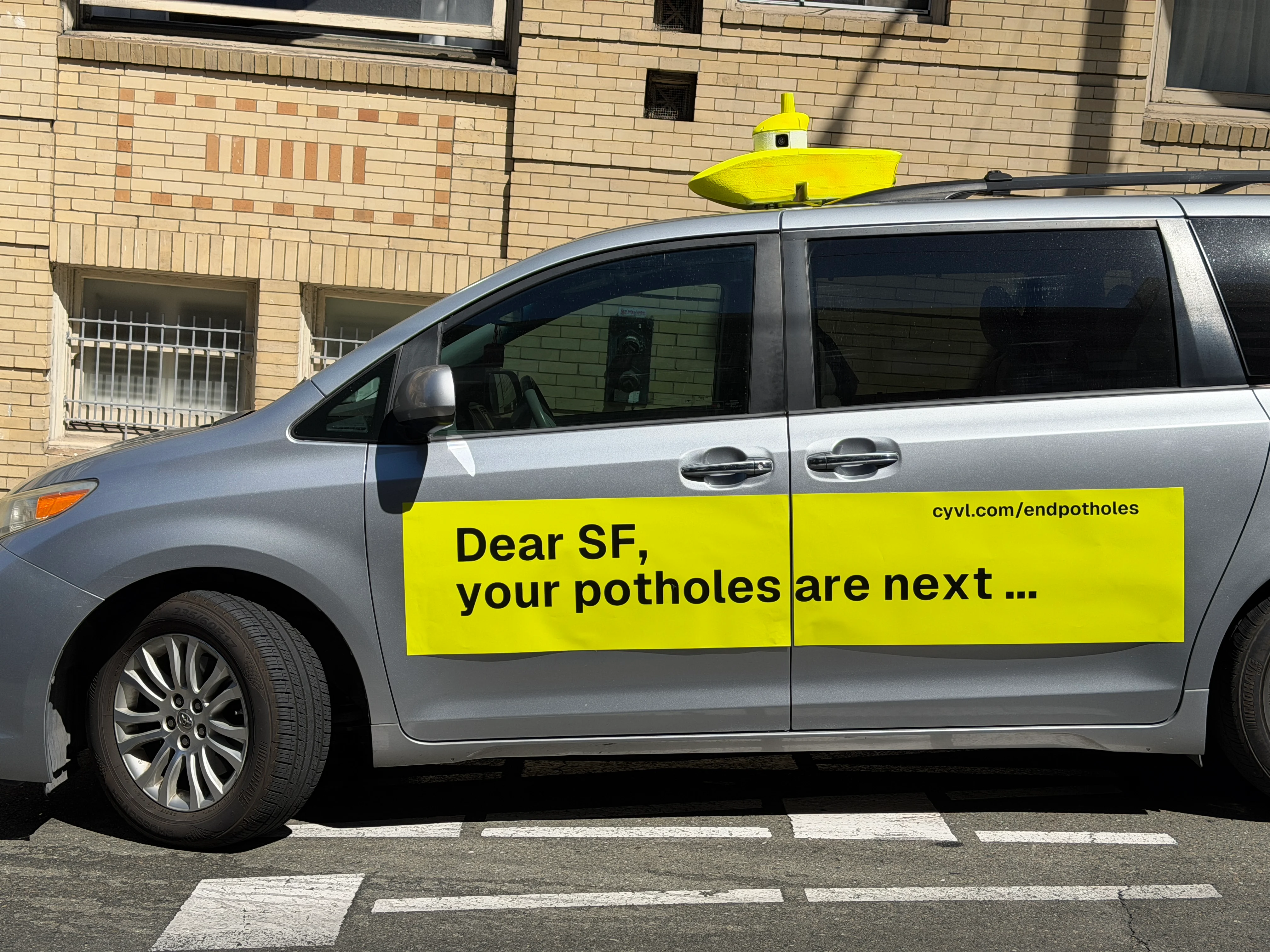 CYVL's silver San Francisco campaign minivan with a yellow pothole sign and roof-mounted sensor