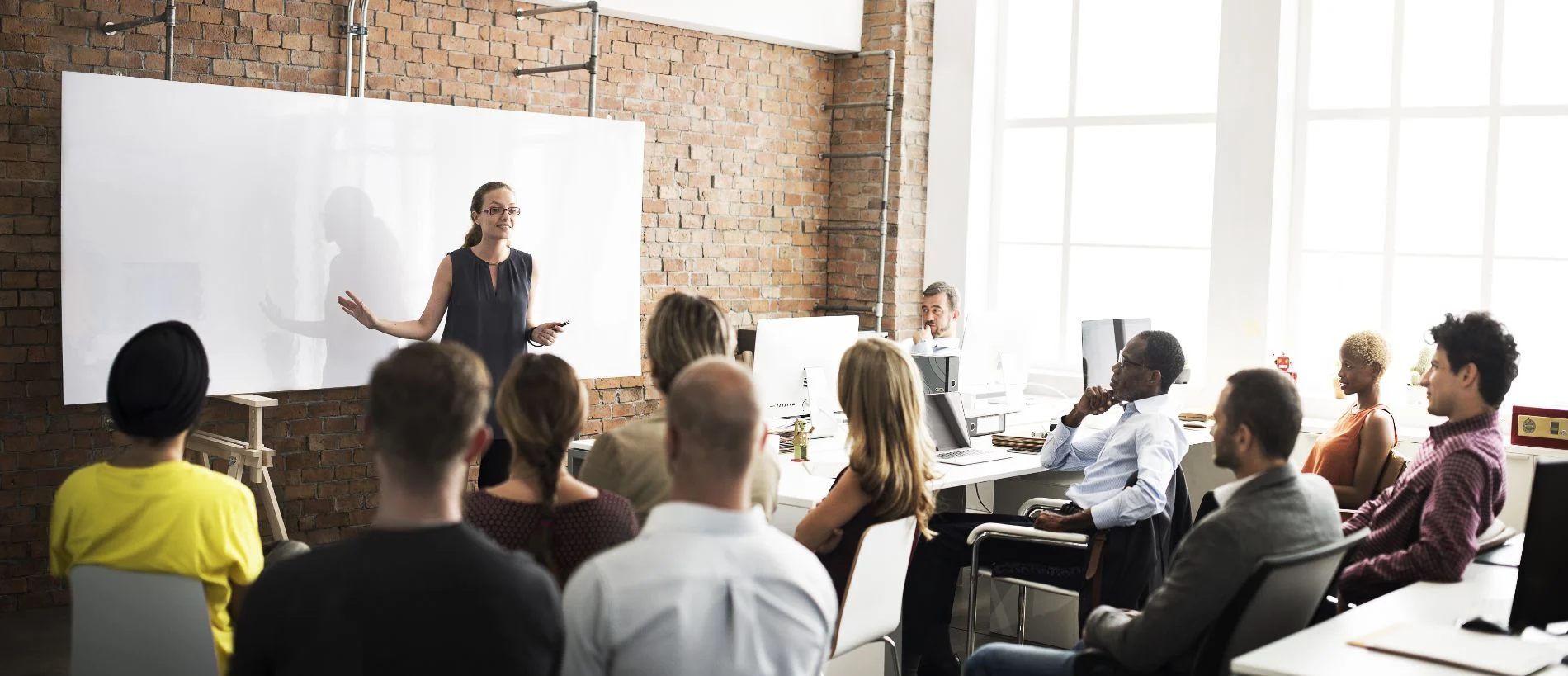 A facilitator presents to a group of colleagues beside a whiteboard