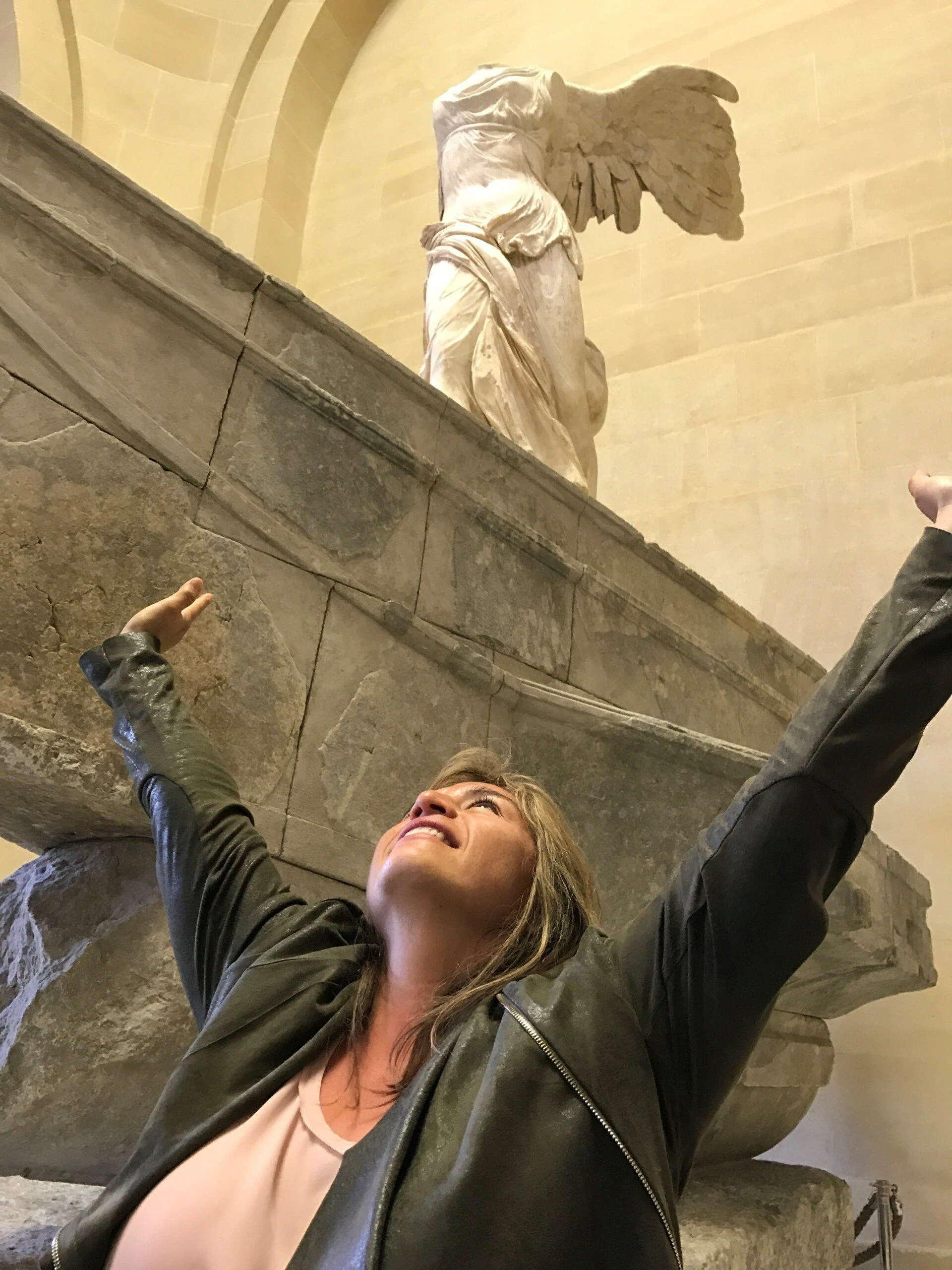 Woman with arms raised beside the Winged Victory sculpture