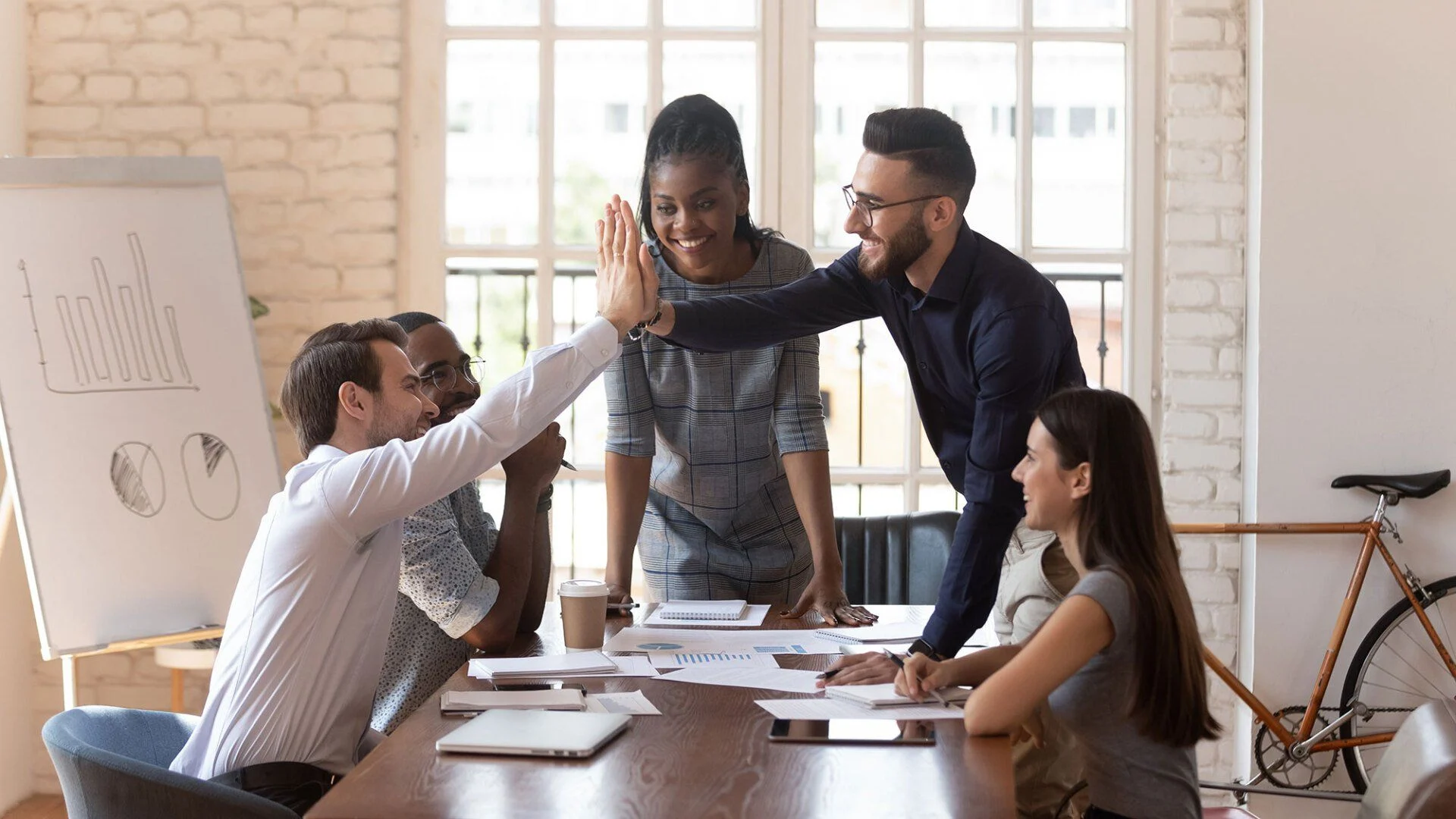 Colleagues share a high five around a conference table