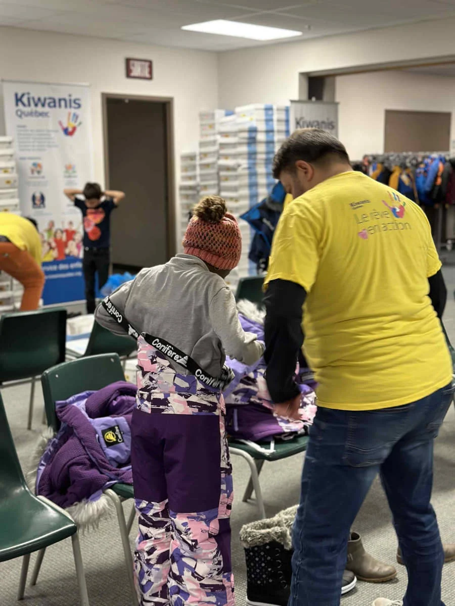 Bénévole du Club Kiwanis de Québec qui aide une enfant à essayer un habit de neige