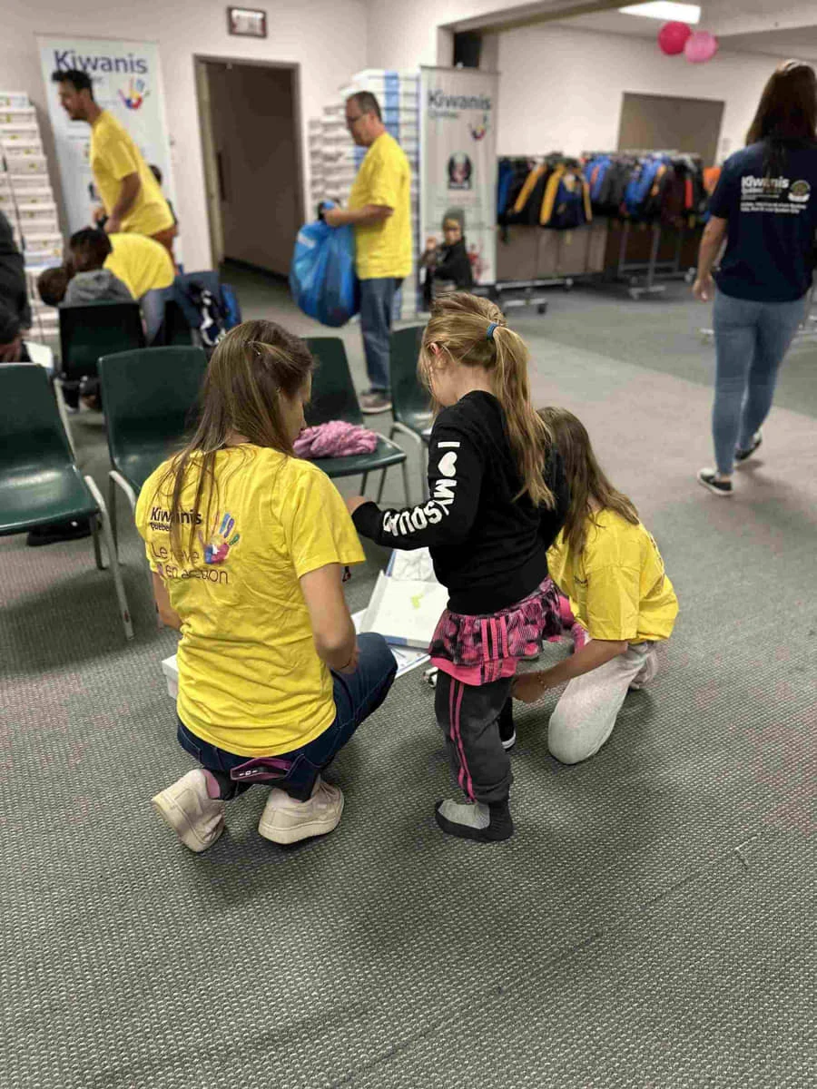 Bénévoles du Club Kiwanis de Québec, en t-shirt jaune, qui aident une enfant à choisir ses vêtements