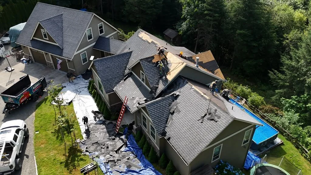 Aerial view of a two-story house mid-reroof, with a crew on the roof and tarps in the yard