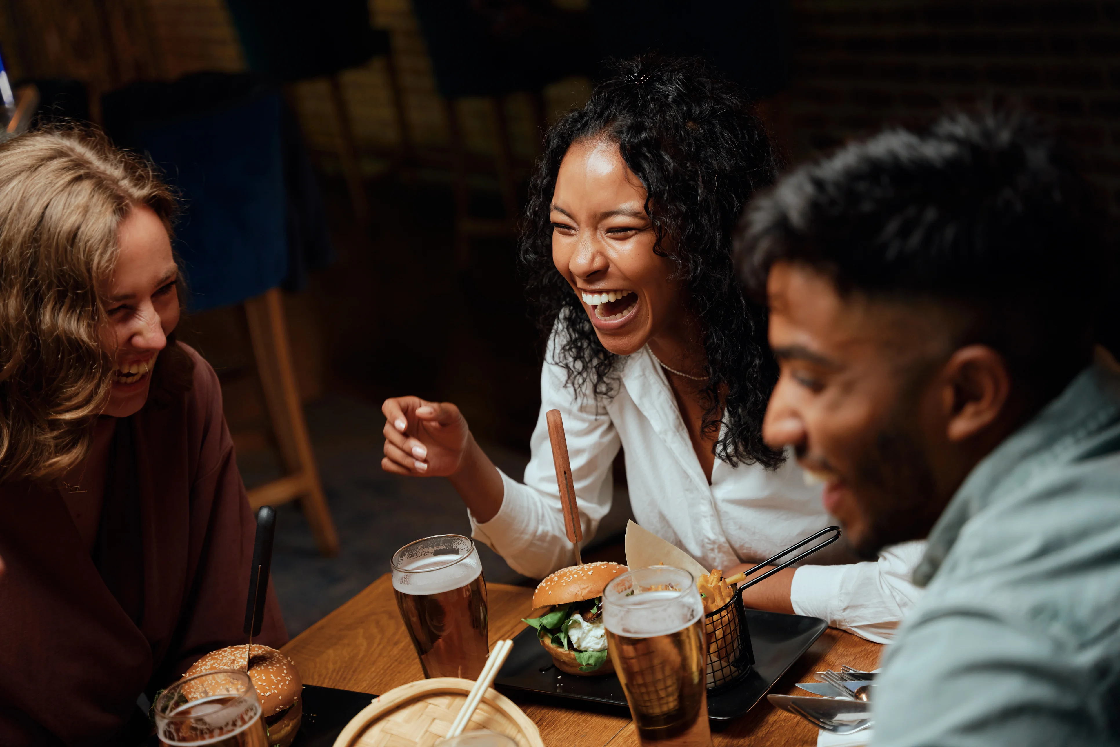 Three friends laughing over burgers and drinks at dinner