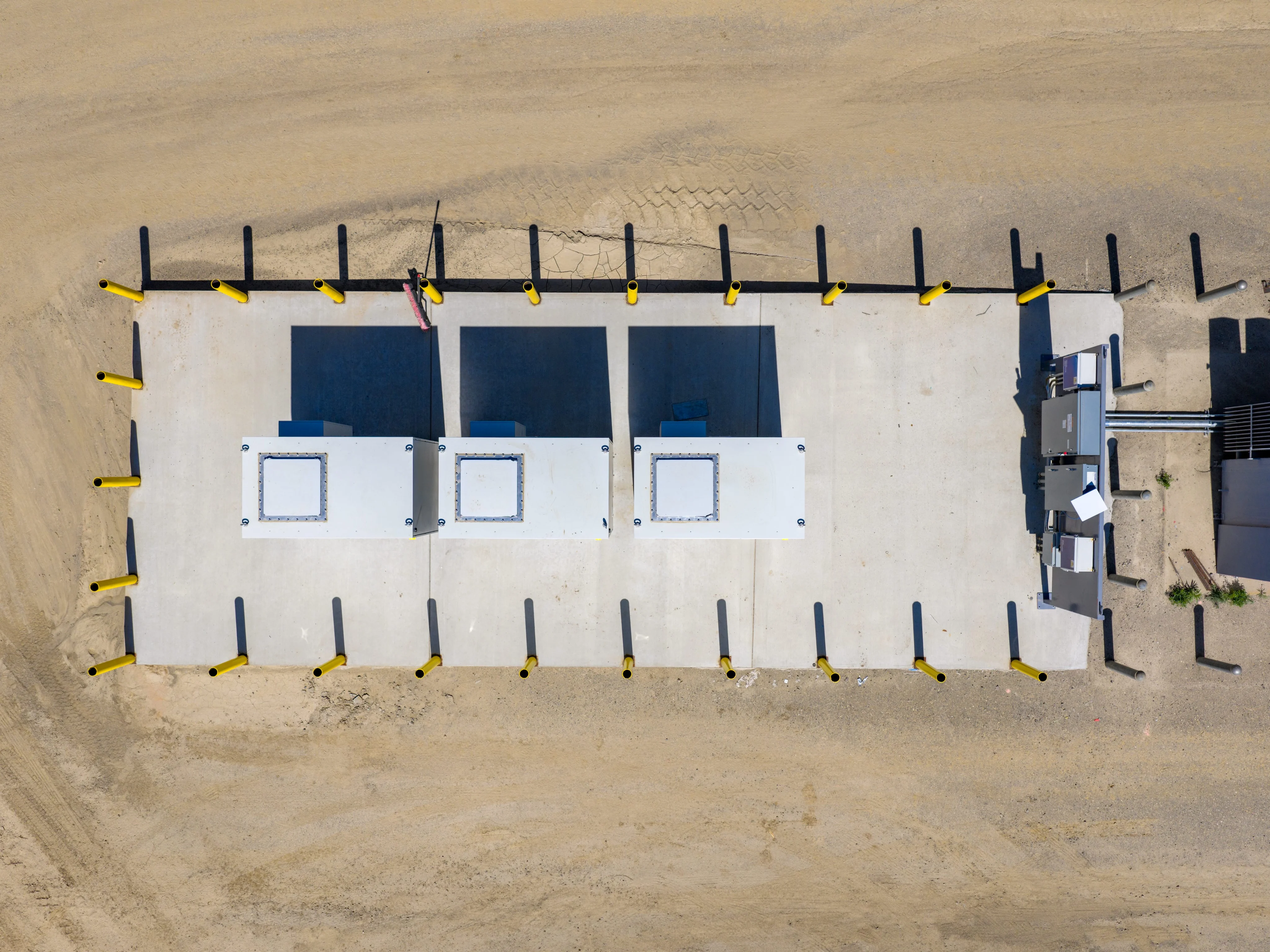 Aerial top-down view of three POSH Station cabinets on a bollard-lined concrete pad next to electrical equipment.