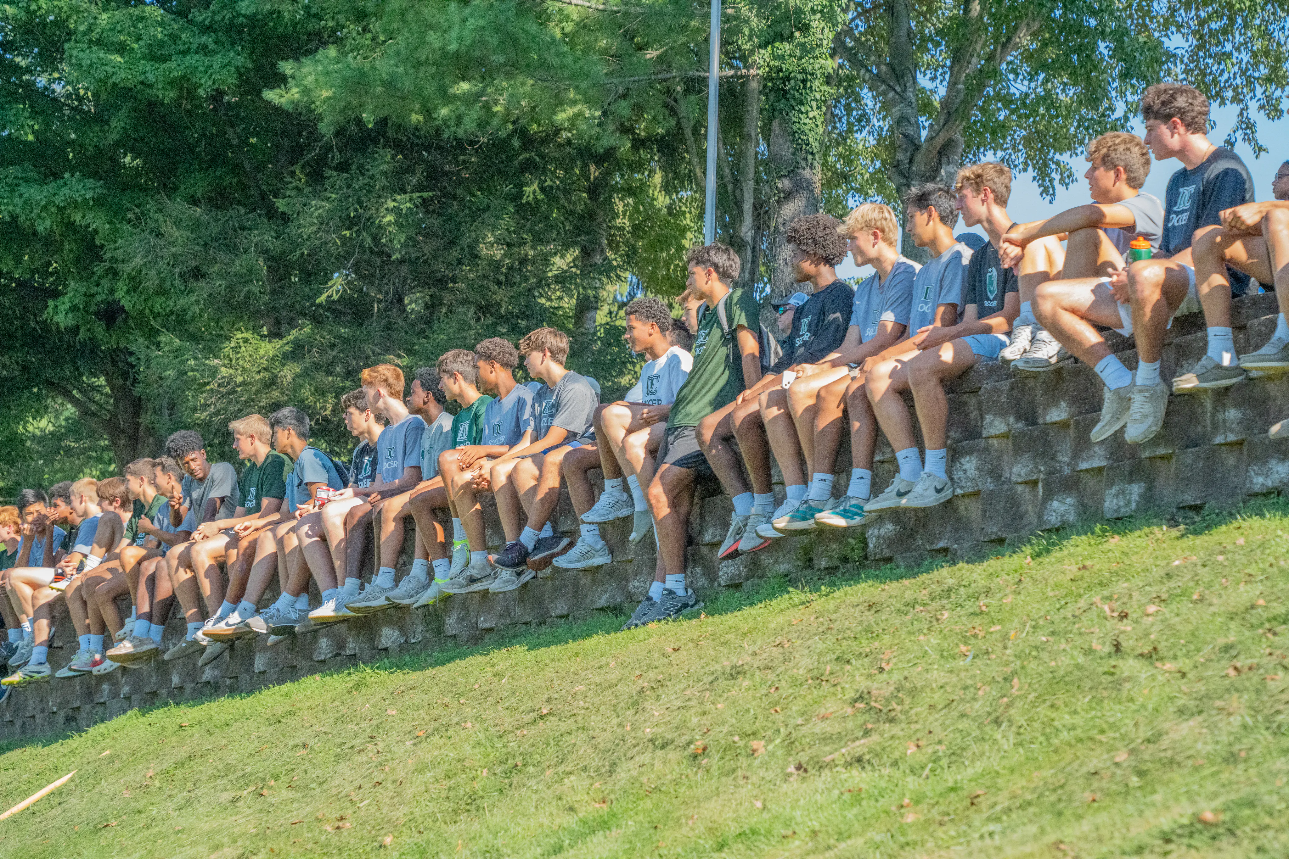 Soccer players seated on a stone wall beside the field