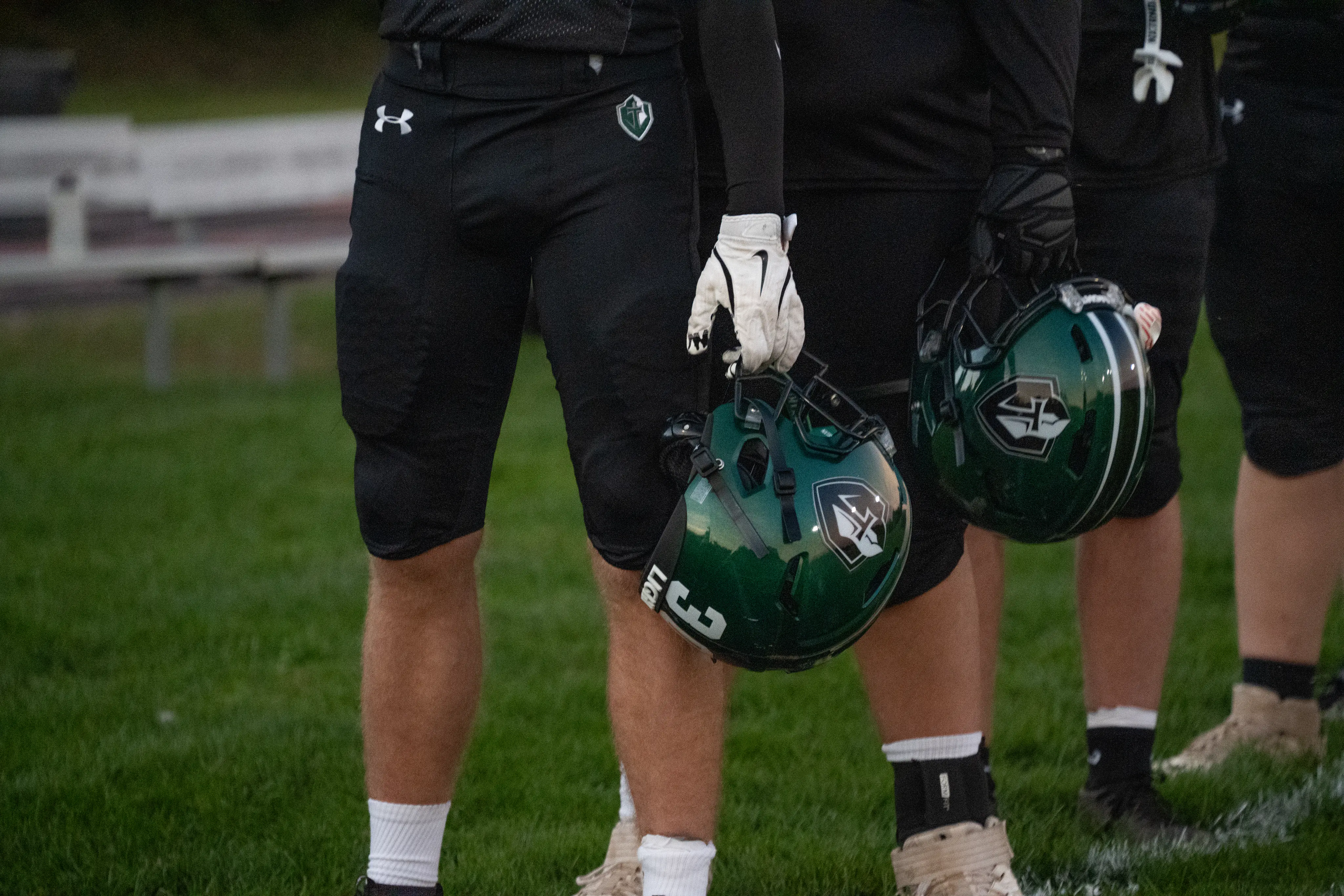 Football players holding green helmets at their sides on the field