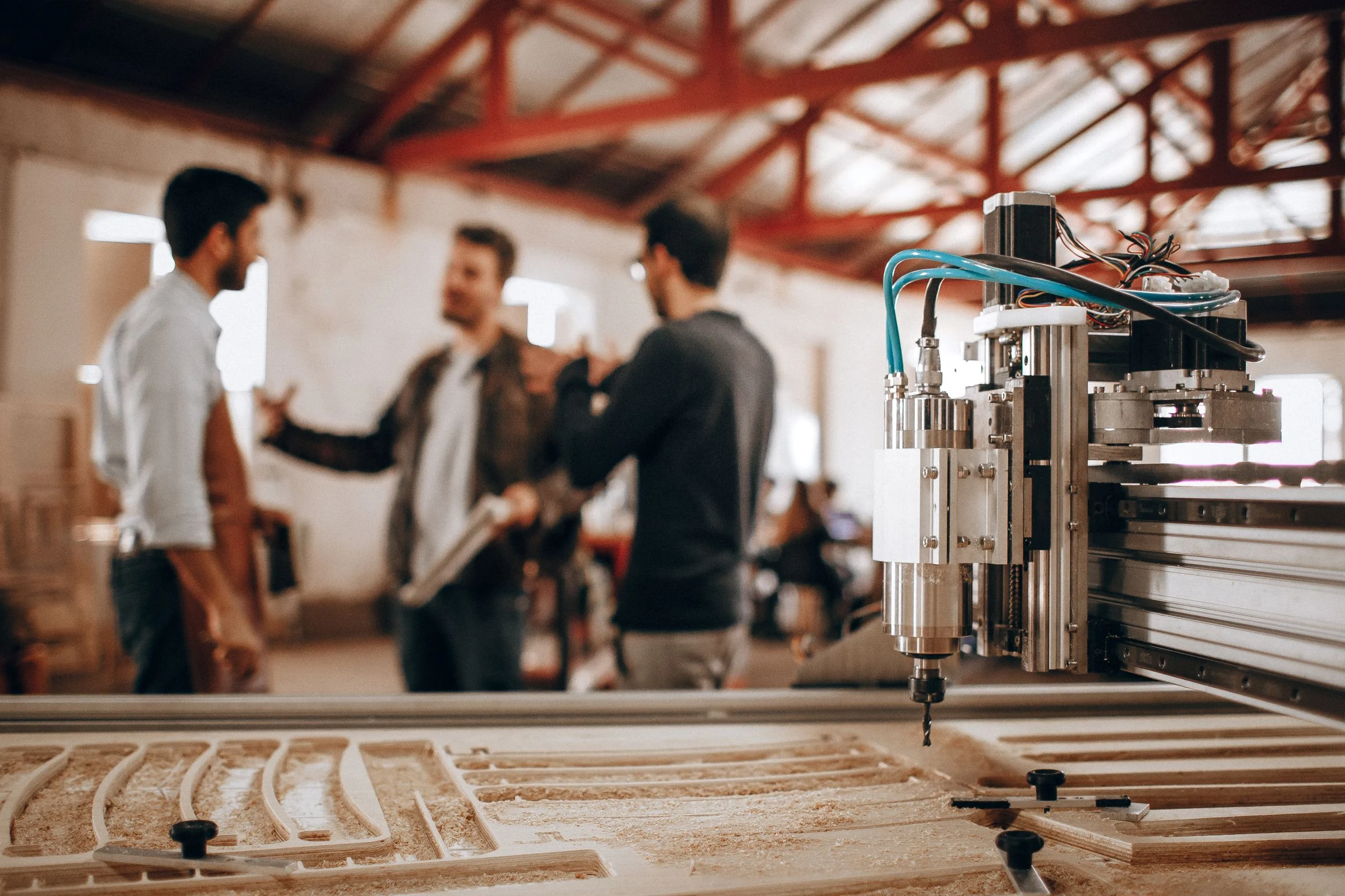 Stock photo of a CNC router cutting wood in a workshop, with workers in the background