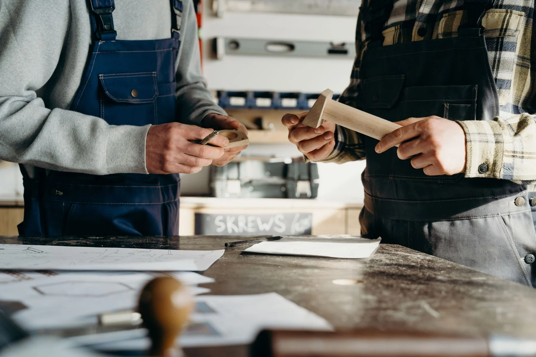 Stock photo of two carpenters reviewing wooden pieces and workshop drawings.
