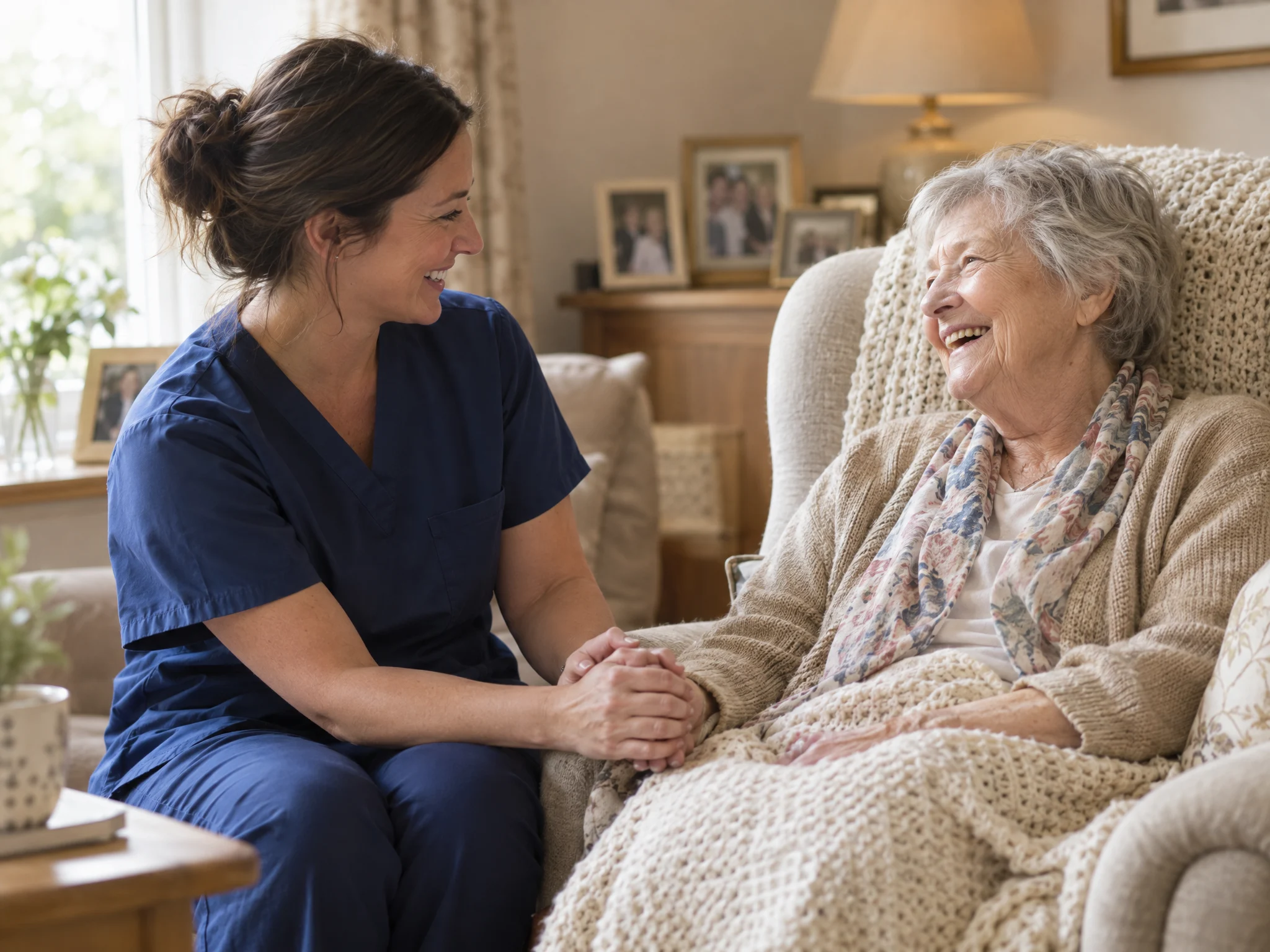 Nurse holding an older woman's hand as they share a laugh in her living room