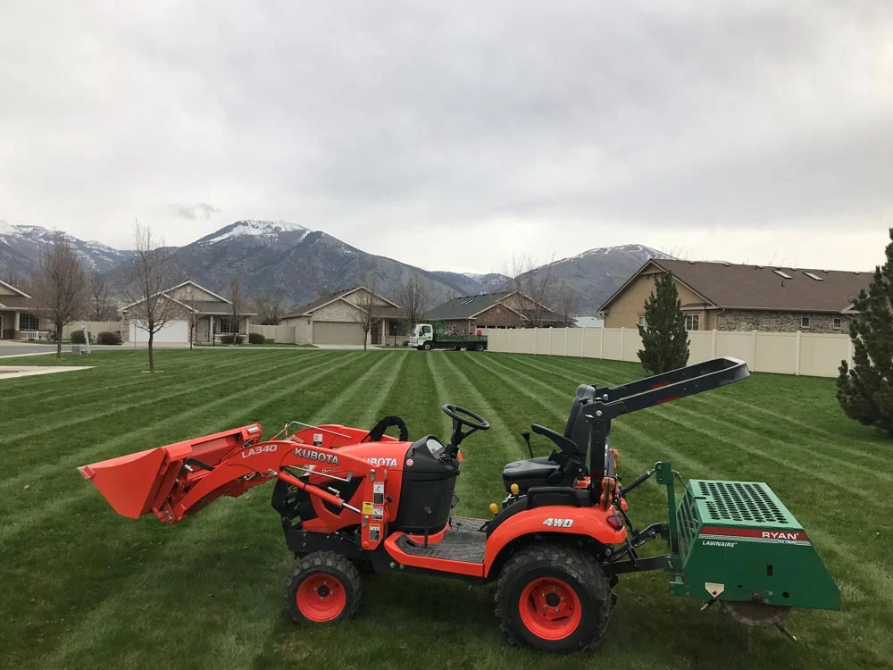 Orange compact tractor on a freshly striped lawn below the mountains