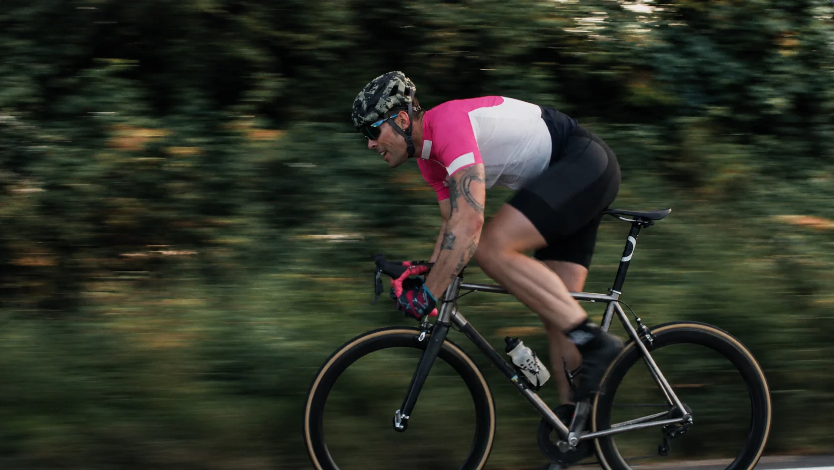 A road cyclist rides at speed past motion-blurred trees.