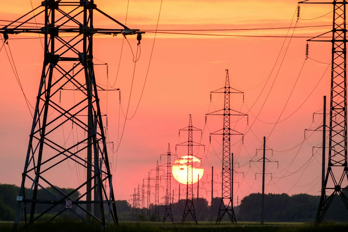 Electricity transmission towers silhouetted against a sunset