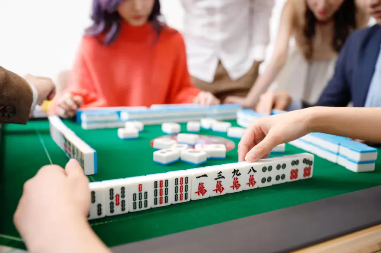 Players arranging Chinese Mahjong tiles around a green table